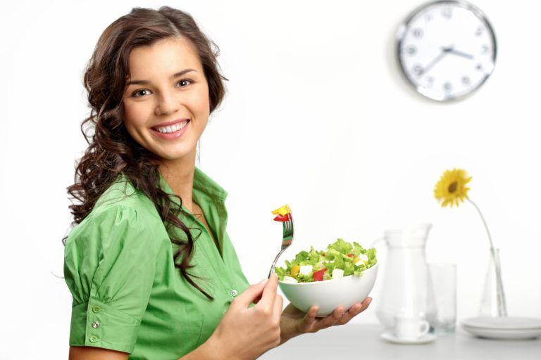 Woman dressed in green eating a salad and smiling